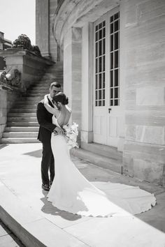 a bride and groom kissing in front of an old building on their wedding day, black and white photo