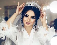 a woman wearing a tiara with feathers around her shoulders and hands behind her head