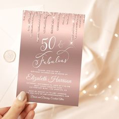 a person holding up a pink and silver wedding card with the word 50 and fabulous written on it