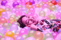 a woman laying in a ball pit with lots of balloons all around her and looking up at the camera