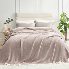 a bed covered in a blanket and pillows next to a potted plant on top of a wooden floor