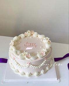 a white cake sitting on top of a table next to a purple ribbon and bow