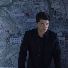 a young man in a black suit standing next to a map