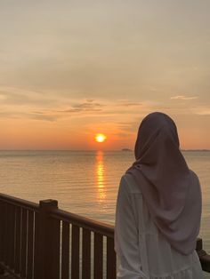 a woman is looking out over the water at sunset