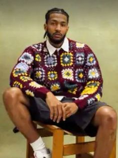 a man sitting on top of a wooden stool wearing a sweater and shorts with colorful flowers