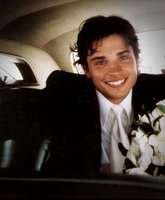 a man in a suit and tie sitting in a car with flowers on his lap