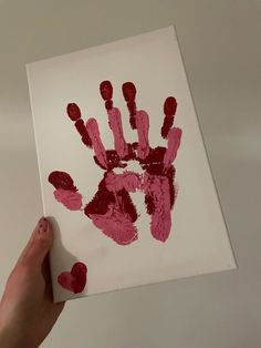 a person holding up a handprint on a piece of paper that has red paint