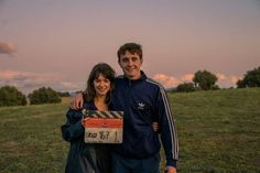 a man and woman standing next to each other in a field holding a sign with the number 1 on it