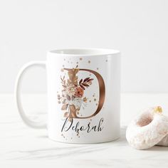 a white coffee mug with the letter d on it next to a half eaten donut