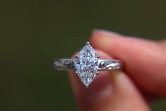 a close up of a person's hand holding a ring with a diamond on it