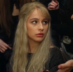 a woman with long blonde hair is looking at the camera while another person looks on