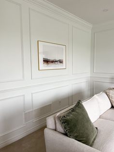 a living room with white paneling and green pillows on the couch, along with a framed painting