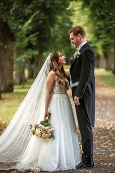 a bride and groom standing in the middle of a path with leaves on the ground