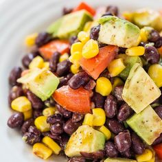 a white plate topped with black beans, corn and avocado salad next to a fork