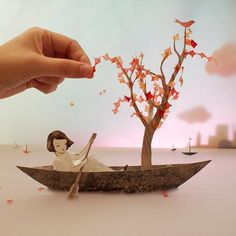 a paper boat with a woman in it floating on the water next to a tree