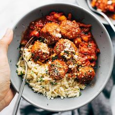 a bowl filled with meatballs and rice on top of a white table next to another plate