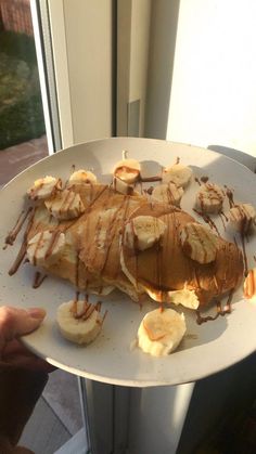 a person holding up a plate with bananas and chocolate syrup on it in front of a window