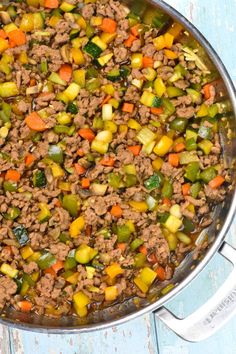 a pot filled with meat and vegetables on top of a blue tablecloth next to a spoon