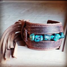 Distressed Finish Leather Cuff features a genuine strand of chunky African Turquoise. Each strand is different and will show varying shades of the natural stone. ***Please view all the pictures as they show examples of the many stone colors Cuff measures 2" by 9" in length Adjustable to 7" and 7.5" Although your item will resemble the photo, each piece is created by hand, so no two are identical.Thank you for visiting The Jewelry Junkie! Adjustable Turquoise Cuff Bracelet With Natural Stones, Southwestern Style Turquoise Leather Bracelet For Festivals, Southwestern Adjustable Cuff Bracelet With Natural Stones, Adjustable Turquoise Bracelets With Patina, Adjustable Turquoise Bracelet With Patina, Adjustable Turquoise Leather Bracelet In Rustic Style, Adjustable Rustic Turquoise Leather Bracelet, Adjustable Bohemian Cuff Bracelet With Natural Stones, Rustic Handmade Turquoise Cuff Bracelet