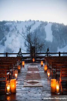 candles are lit in front of rows of wooden chairs on a deck overlooking a snowy mountain