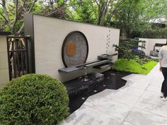 a woman walking down a sidewalk next to a water feature in the middle of a garden