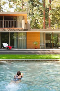 a woman swimming in a pool next to a large house with glass doors and windows