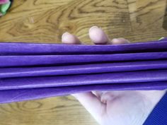 a person holding up purple sticks on top of a wooden table