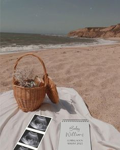 a basket with baby pictures sitting on top of a blanket next to the ocean and beach