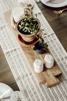 the table is set with white dishes and plates, including two small pots filled with plants