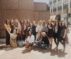 a group of women standing next to each other in front of a brick wall and building