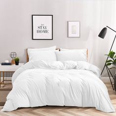 a bed with white comforter and pillows in a room next to a lamp on a table