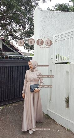 a woman wearing a hijab standing in front of a white building with a black fence