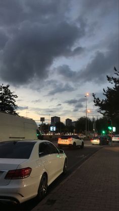 cars are parked on the side of the road under dark clouds and green traffic lights