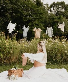 a woman sitting on top of a blanket next to a basket filled with laundry hanging from clothes line