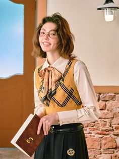 a woman wearing glasses and a bow tie standing in front of a brick wall holding a book