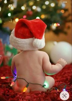 a baby wearing a santa hat sitting in front of a christmas tree with lights on it