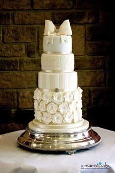 a three tiered wedding cake with white flowers and bows on the top is sitting on a silver platter