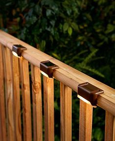 three lights are on the side of a wooden deck railing with trees in the background