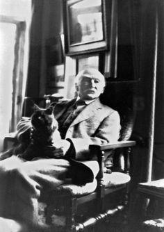 an old black and white photo of a man sitting in a chair with his dog