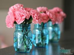 three mason jars filled with pink carnations on a table