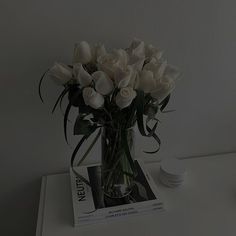 a vase filled with white roses sitting on top of a table next to a book