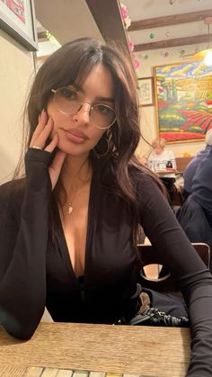 a woman sitting at a table with her hand on her head and wearing glasses, posing for the camera