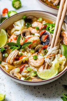 two bowls filled with shrimp and noodle soup next to chopsticks on the side