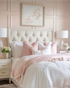 a white bed with pink pillows and blankets in a room that has light pink walls