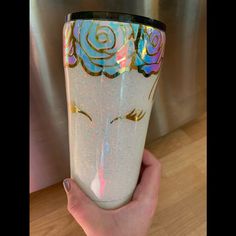 a hand holding a cup with an image of a rose on the side and gold glitter