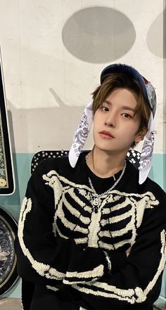 a young man sitting on top of a bench wearing a skeleton sweater and bandana