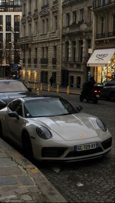 two cars parked next to each other on the side of a road near tall buildings