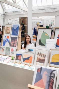 a woman is standing in front of some art on display at an art fair,