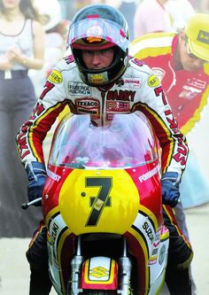 a man riding on the back of a red and yellow motorcycle in front of people