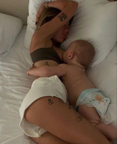 a woman laying on top of a bed next to a baby in a diaper